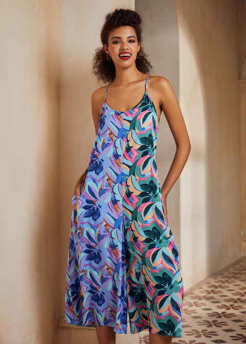 Woman wearing a colorful floral dress standing against a neutral wall.